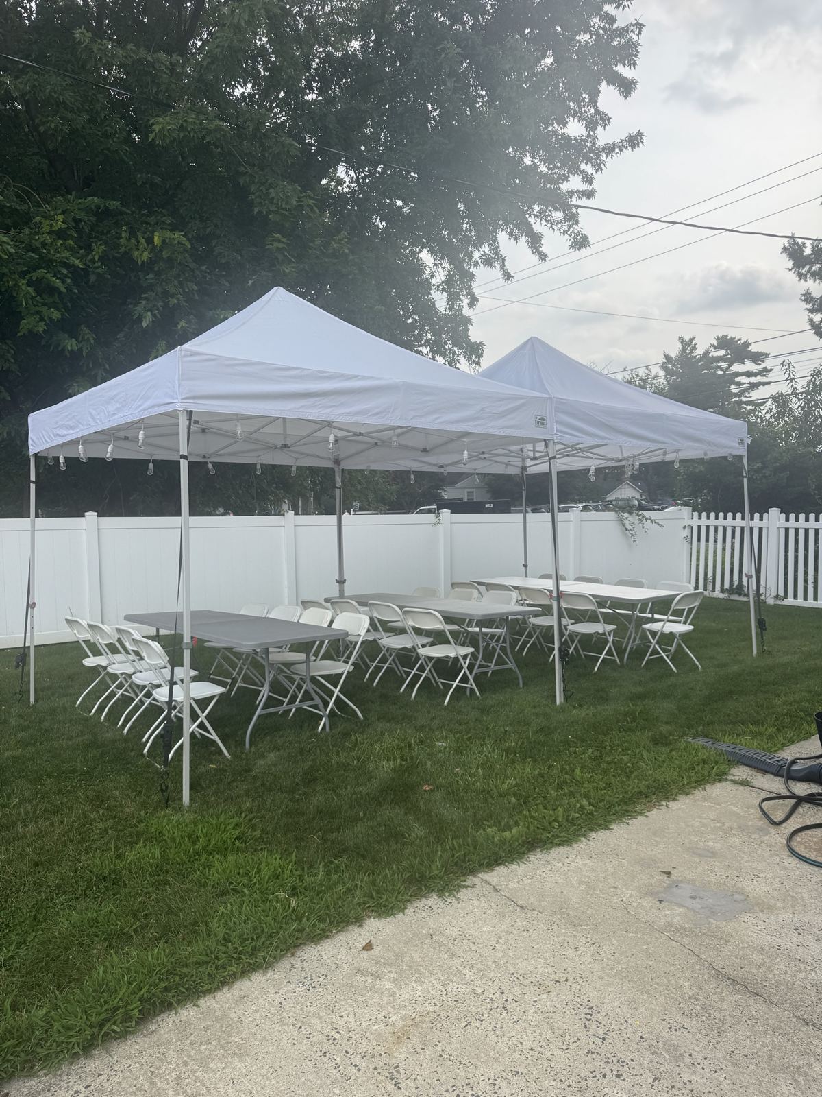 Two pop-up tents with string lights over banquet tables and white folding chairs